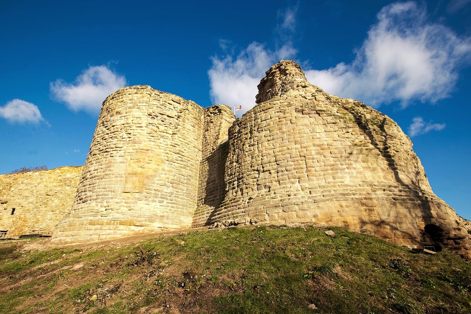 The stone towers and ruined walls of Pontefract Castle rising above a grassy bank