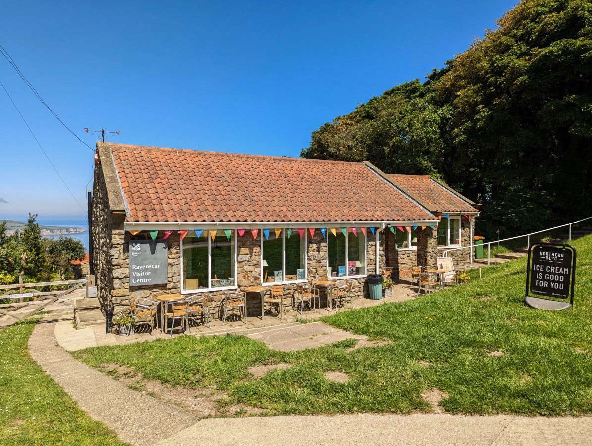 The National Trust visitor centre at Ravenscar, a low stone building with bunting and outdoor tables, sea and cliffs beyond