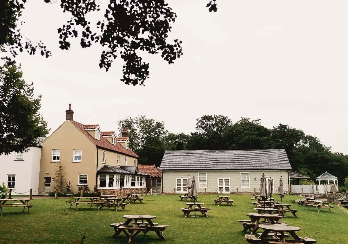 The Boathouse at Ormesby seen across its lawn, wooden picnic tables set out in front of the pale rendered building