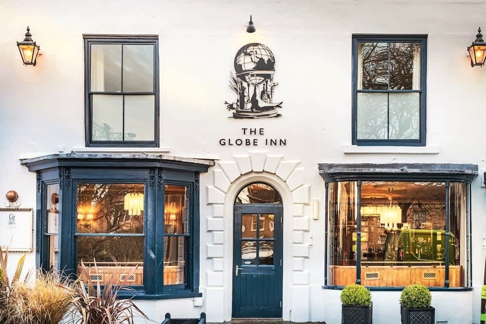 The white frontage of the Globe Inn at Wells-next-the-Sea, with dark bay windows, outdoor tables and planters along the front